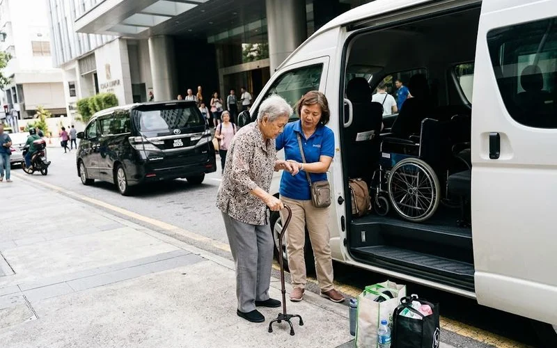 An elderly traveller being helped into a tour vehicle by a driver, with a family member nearby