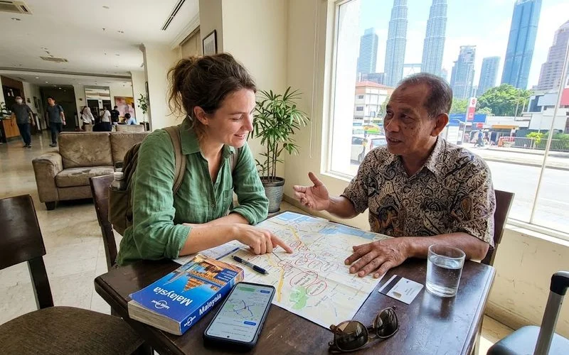 A first-time visitor studying a Kuala Lumpur city map with a guidebook and phone at a hotel desk